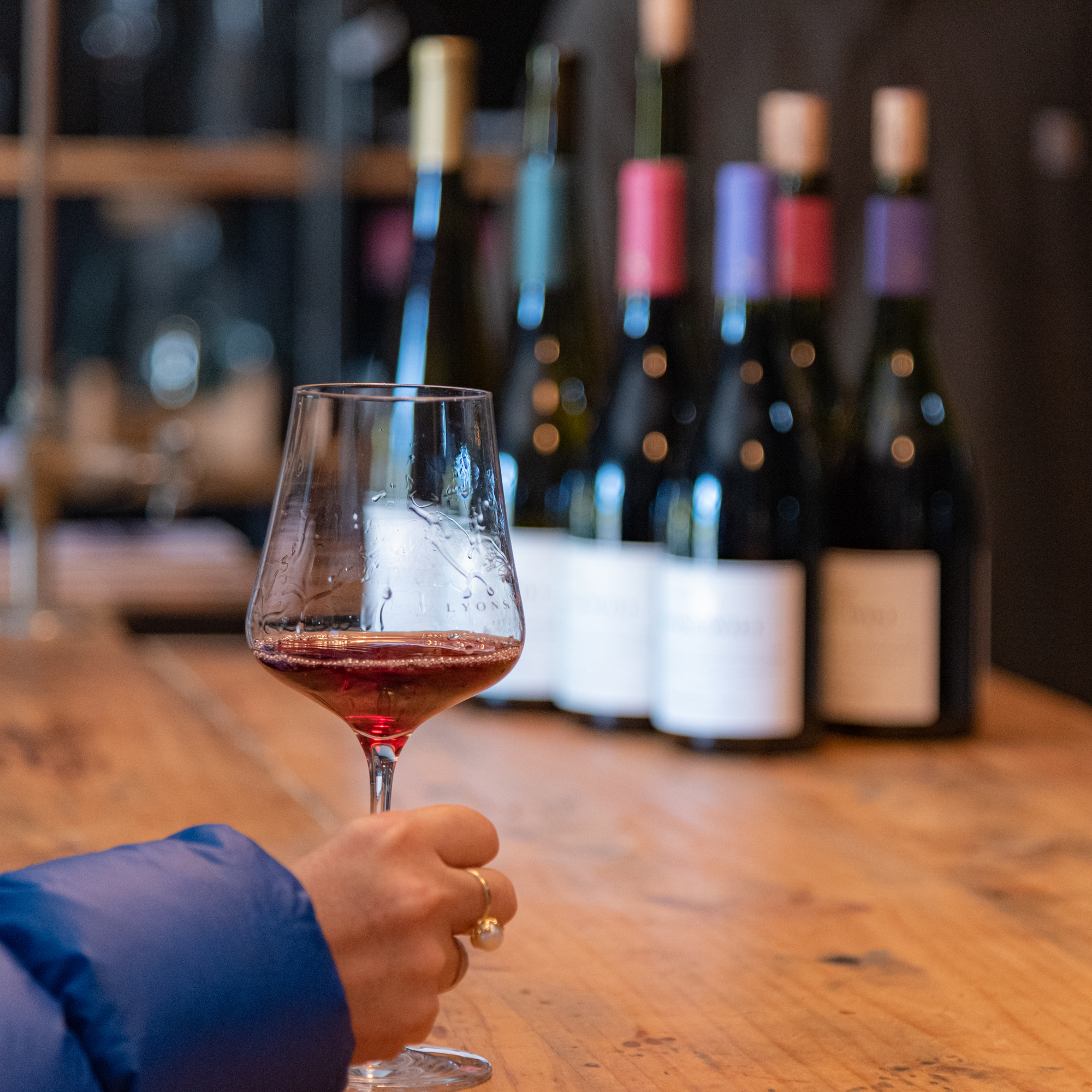 Wine bottles on table and man's hand holding wine glass with wine 